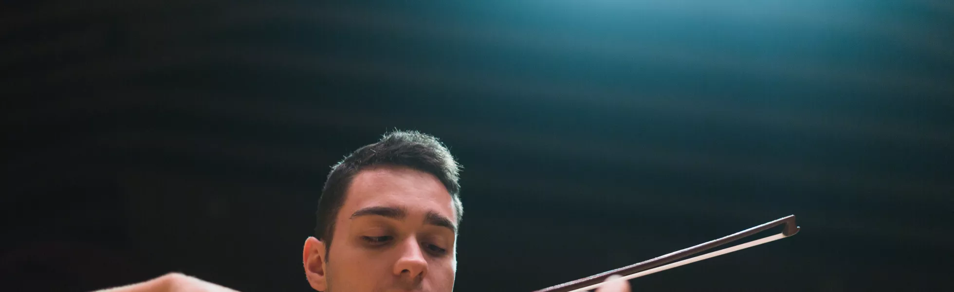 A student playing a violin on a stage under lights.