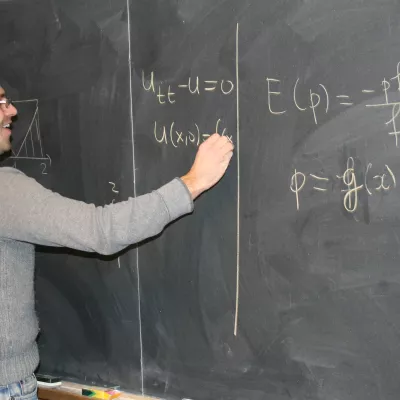 A student writing statistic equations on a blackboard with chalk.