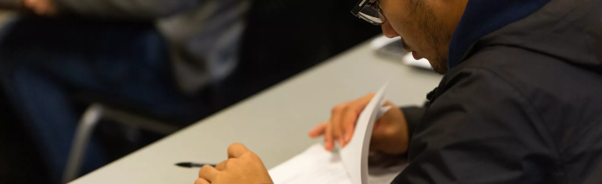 A student sitting at a table looking over papers with a calculator next to him.
