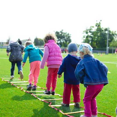 A row of children wearing coats playing outside on green grass.