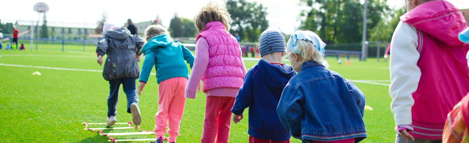 A row of children wearing coats playing outside on green grass.