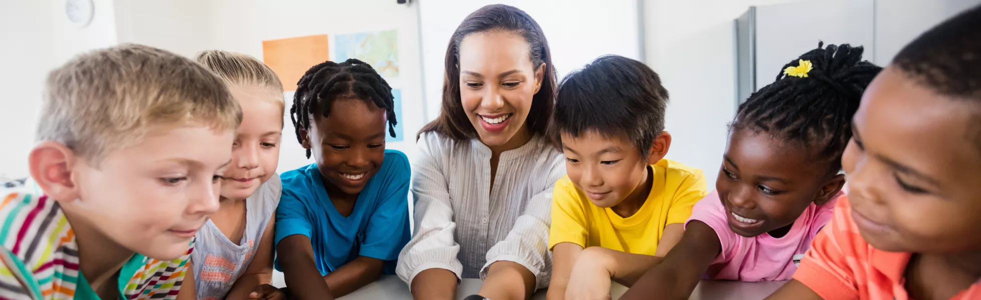 Elementary Students gathered around an elementary school teacher looking at a tablet computer.