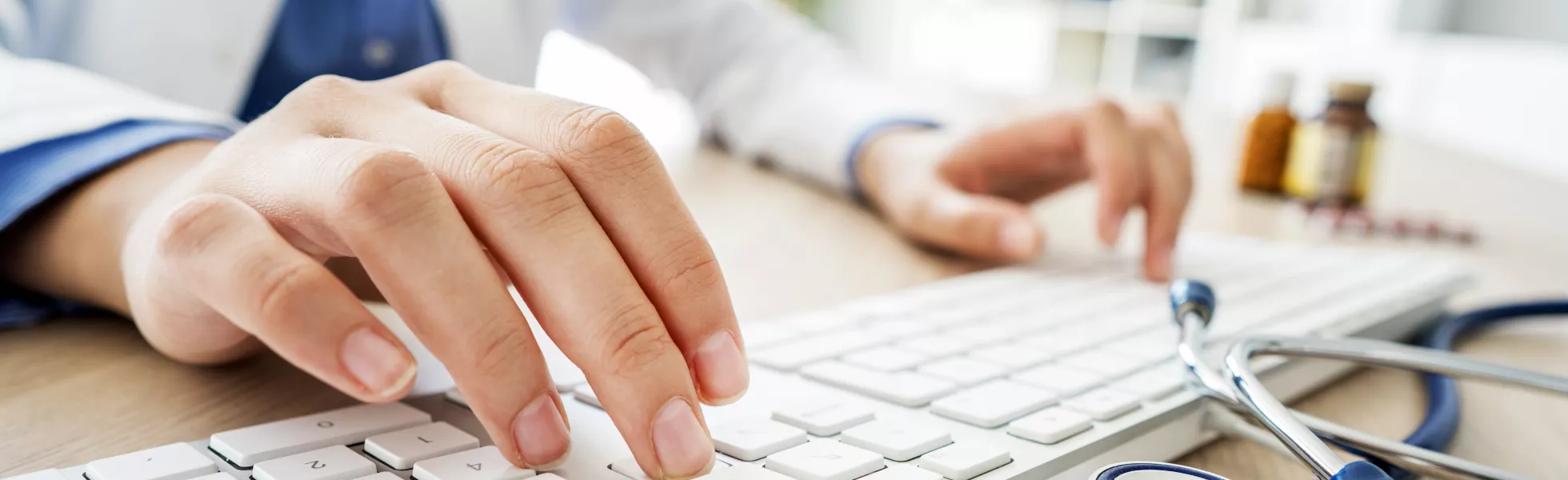 Close-up of a medical professional typing on a keyboard with a stethoscope next to them.