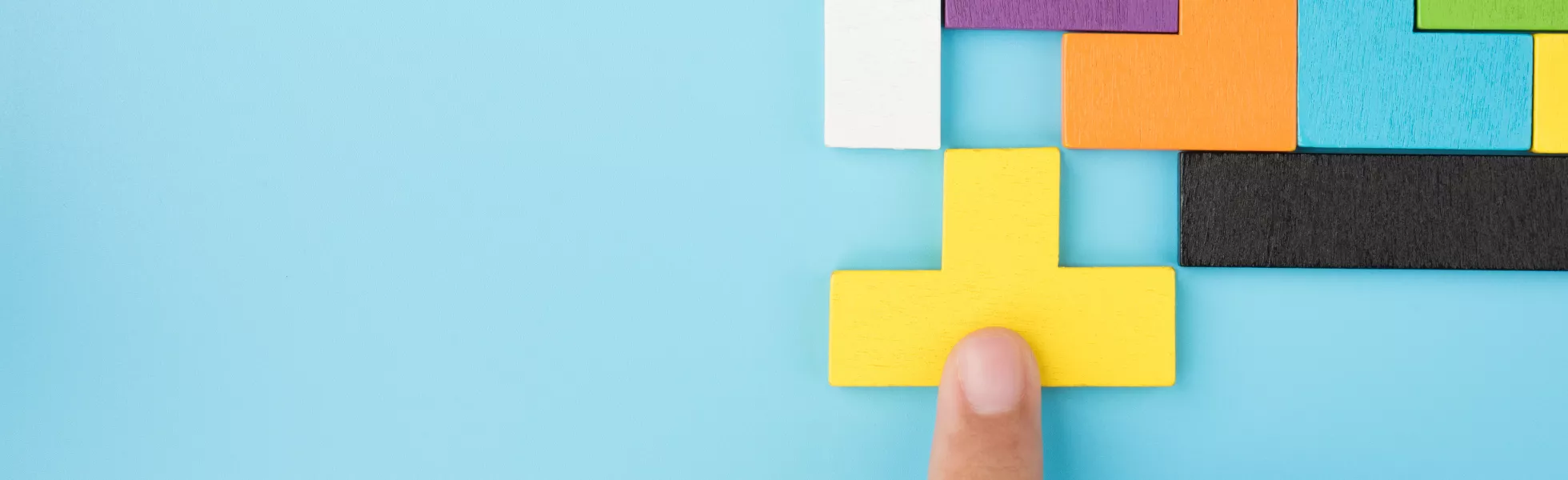 A hand pushing a yellow shape into place in a group of colored shapes.
