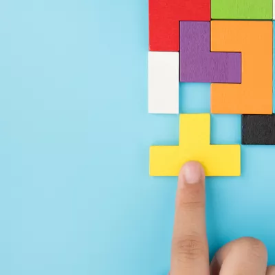 A hand pushing a yellow shape into place in a group of colored shapes.