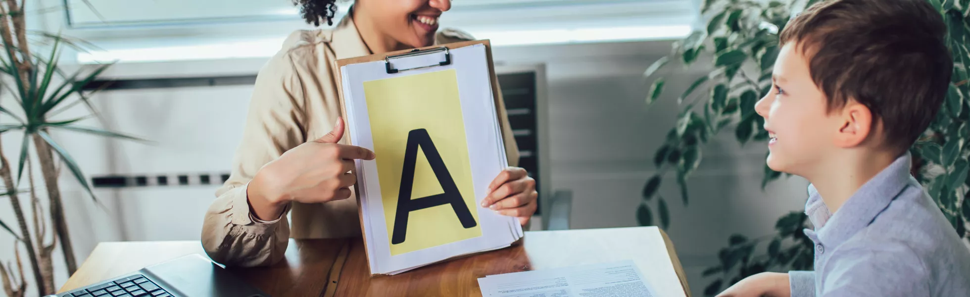A teacher and a student talking, the teacher is holding up a piece of paper with a large letter A.