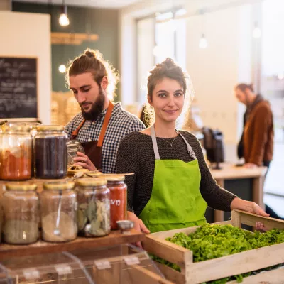 Two store owners displaying food products in their business.