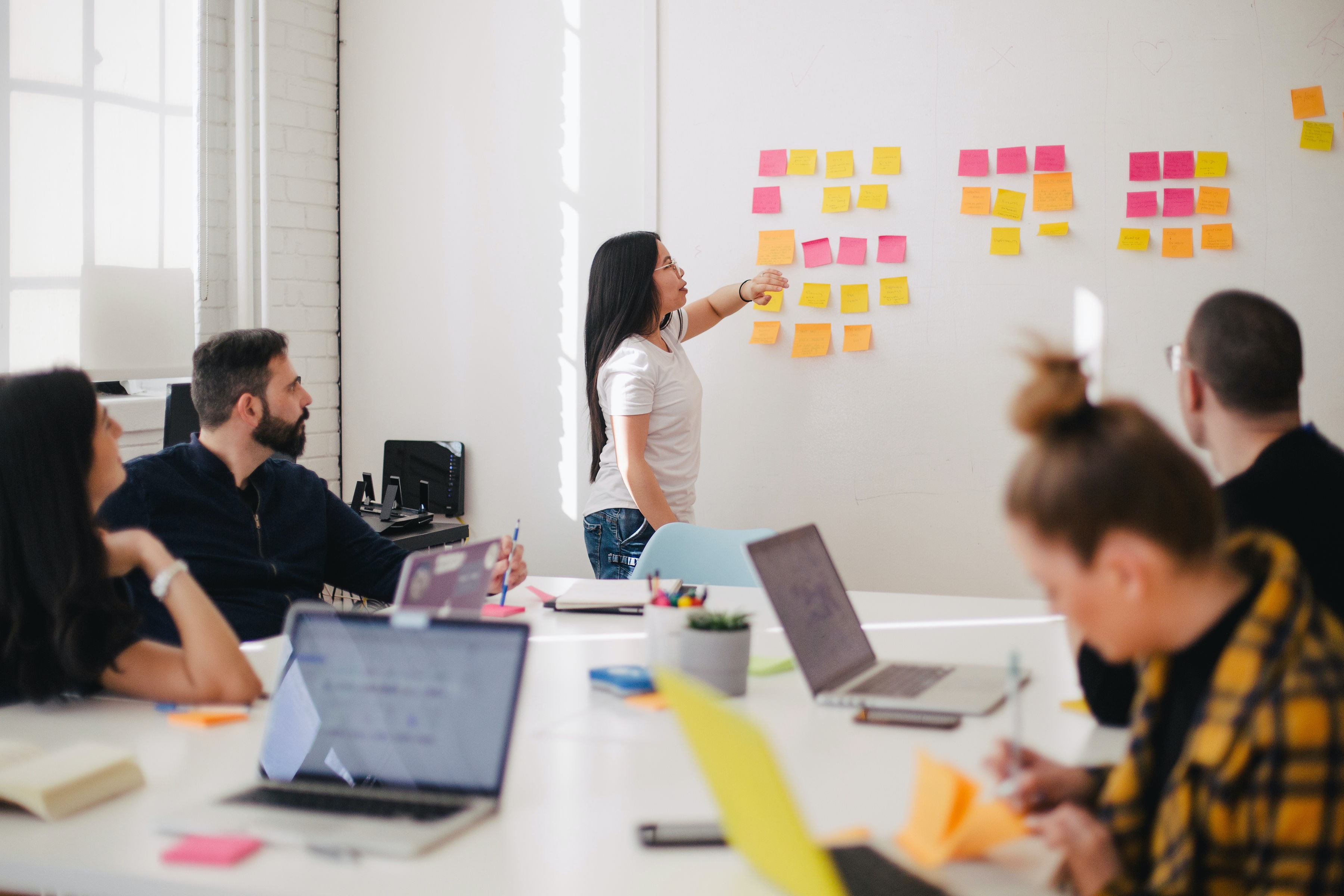 A woman presenting a board full of post it notes to a table full of people