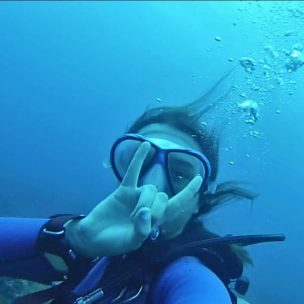 Amirah Casey underwater with her scuba gear on and holding up the "horns" gesture commonly used among students to show WWU Vikings school spirit.