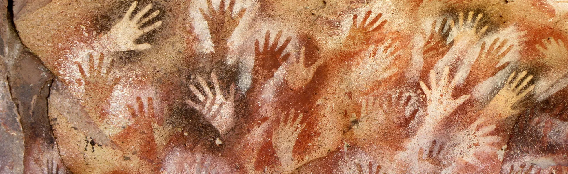 Hand stencil cave paintings cover the walls of a cave in white, black, red, and brown pigment.