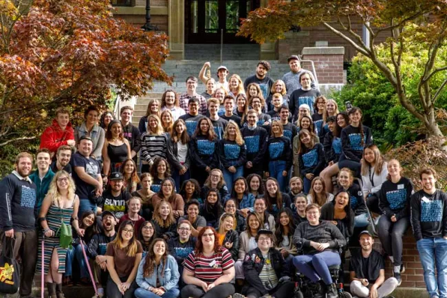 A large group of Associated Student employees sit outside on the steps of Old Main