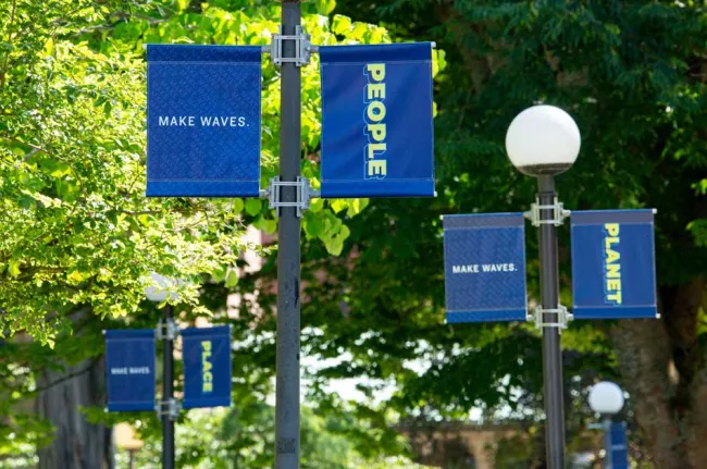 Three light post banners line the walkway leading to Old Main reading People, Planet, Place.