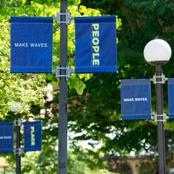 Three light post banners line the walkway leading to Old Main reading People, Planet, Place.