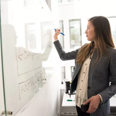 A person writing on a white board during a presentation.