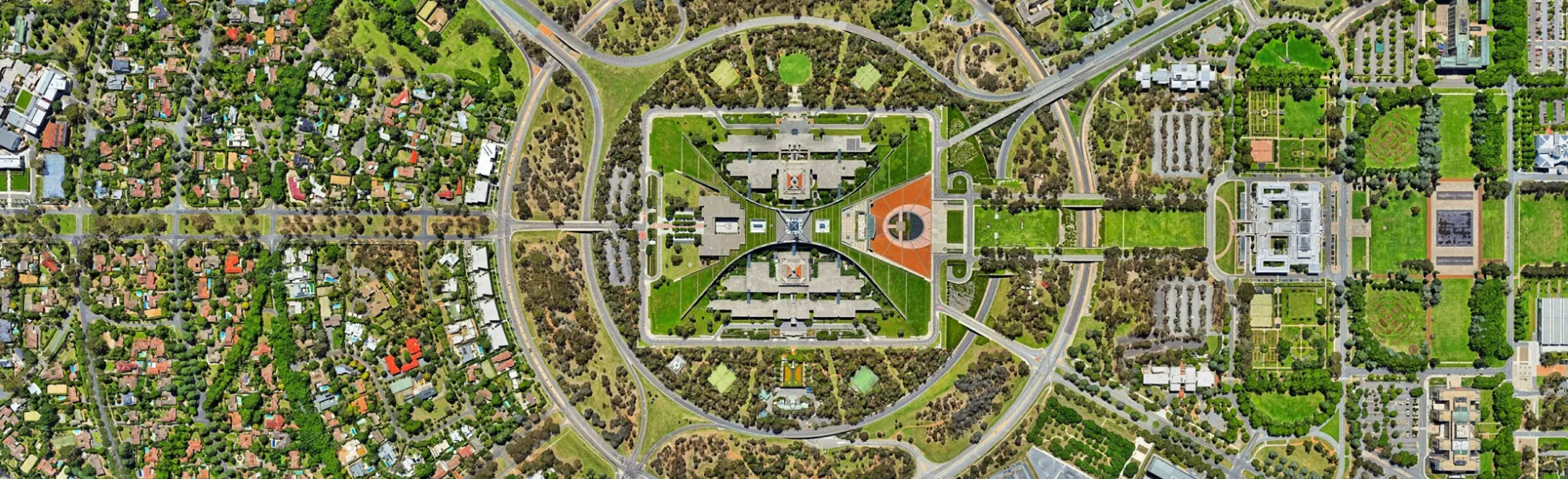 Aerial view of the Canberra Parliament House, Australia. A large green rectangular campus with large boomerang walls surrounding parliament buildings. All surrounded by concentric circles of roads. The parliament is clearly what the rest of the city revolves around.