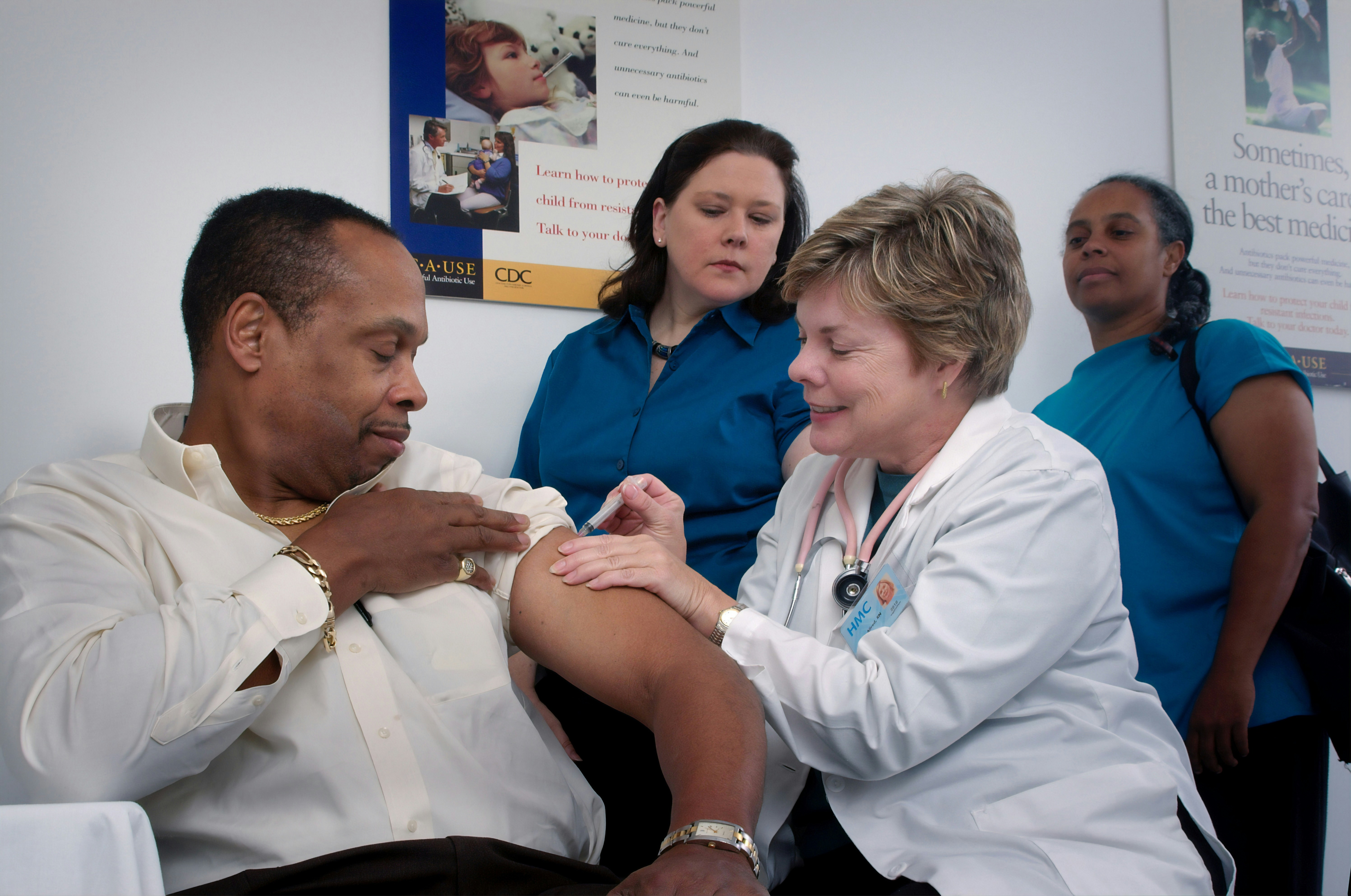 A doctor giving a man a shot, while two nurses look on