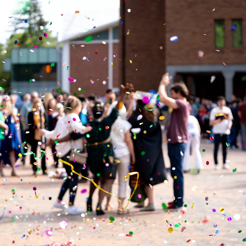 A group of people celebrating in WWU Red Square behind confetti tossed in the air