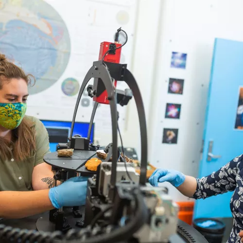 A student and instructor work on a machine holding several pieces of rock.