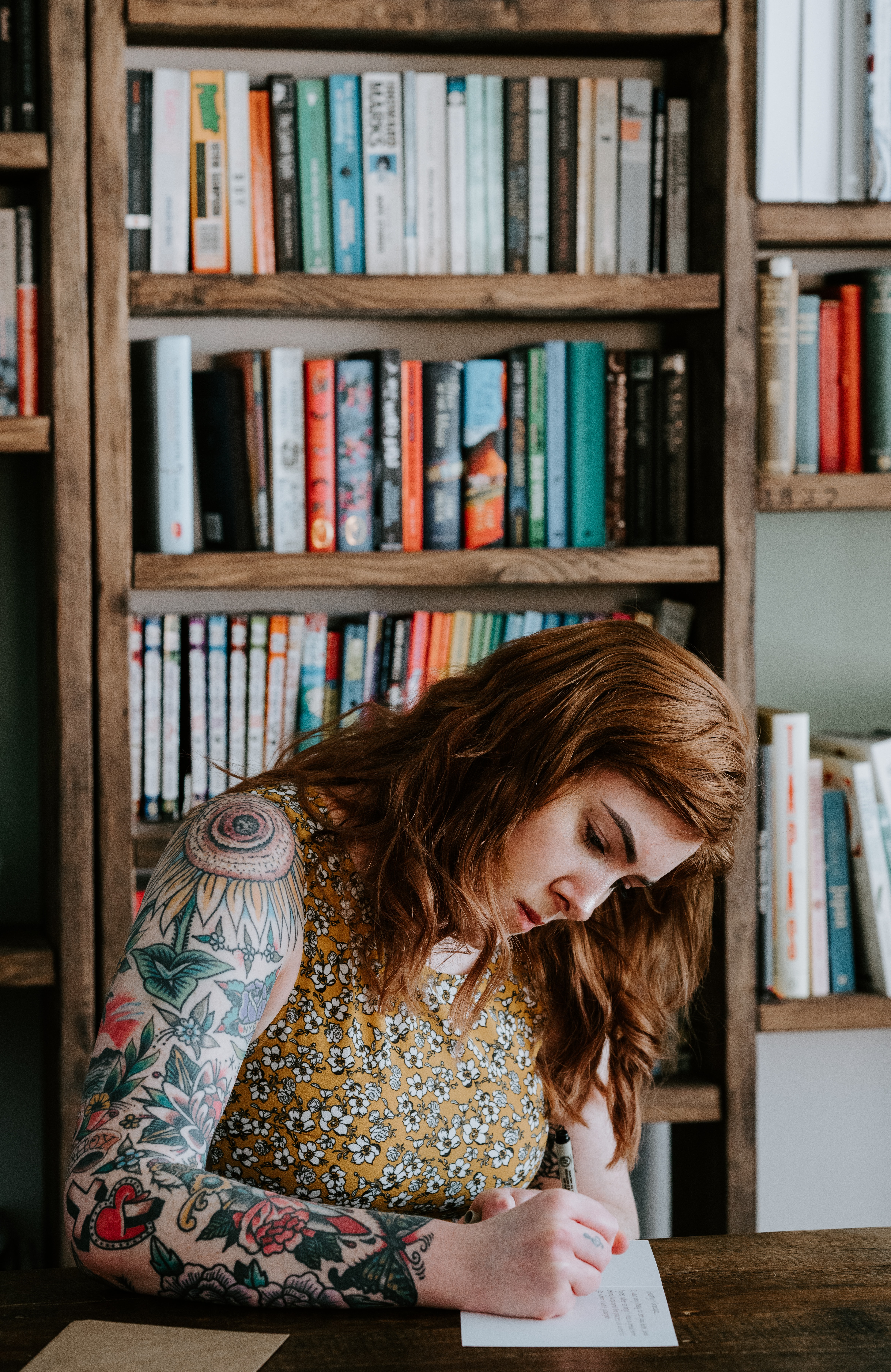 A woman sitting in front of a shelf full of books writing with a pen