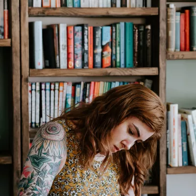A woman sitting in front of a shelf full of books writing with a pen