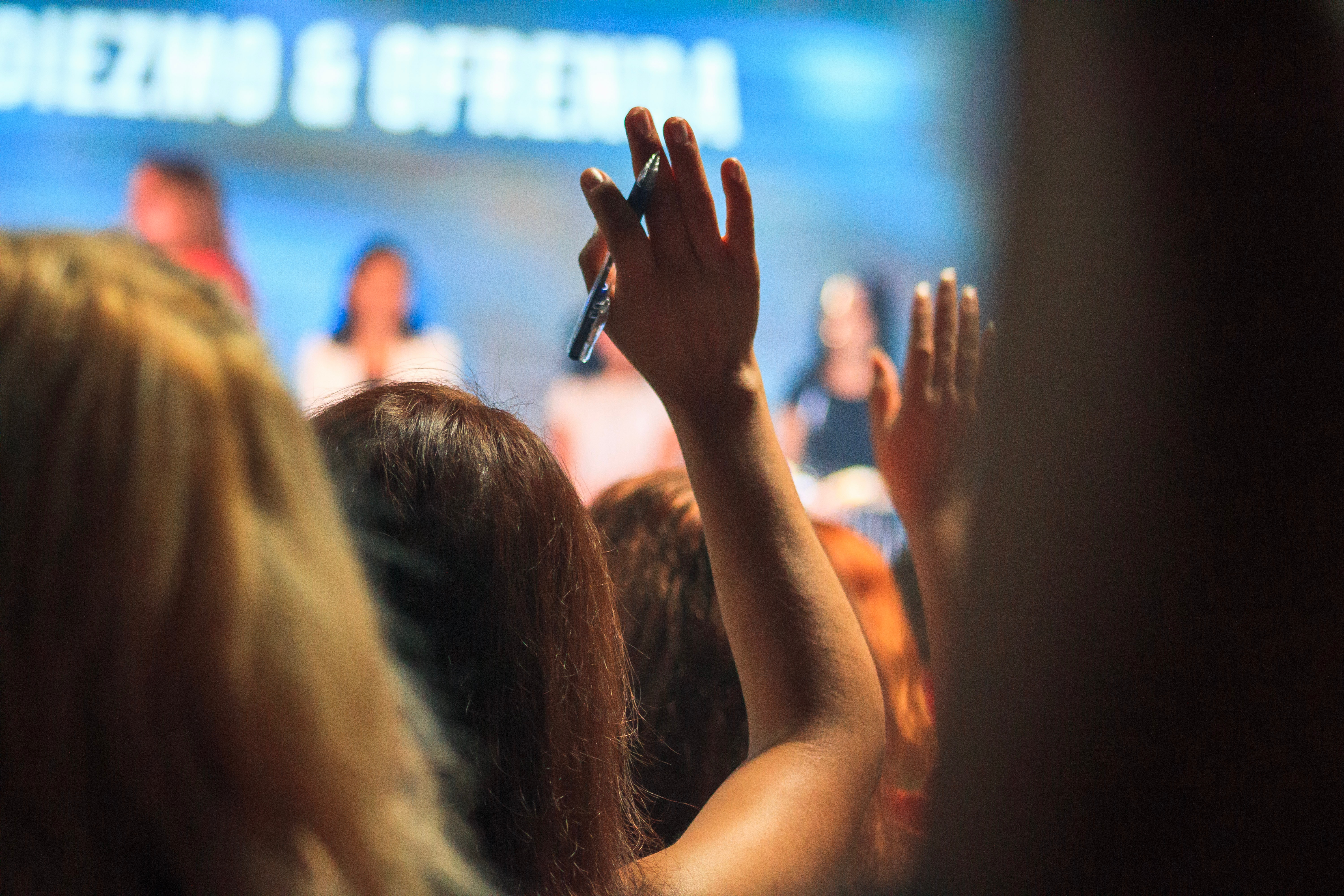 Back view of someone in an audience with their hand up