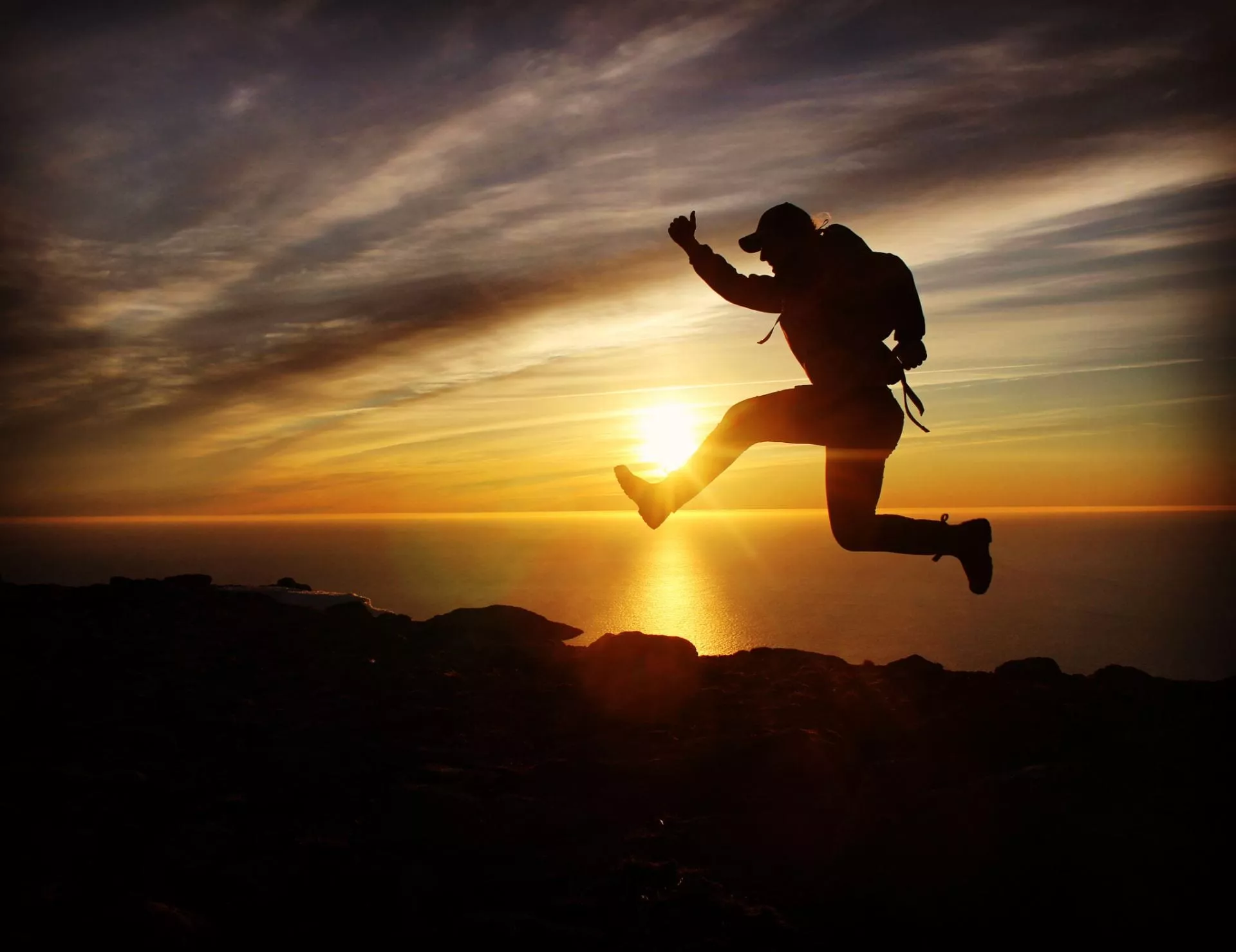A student silhouetted by sunlight jumping joyously along a hilltop