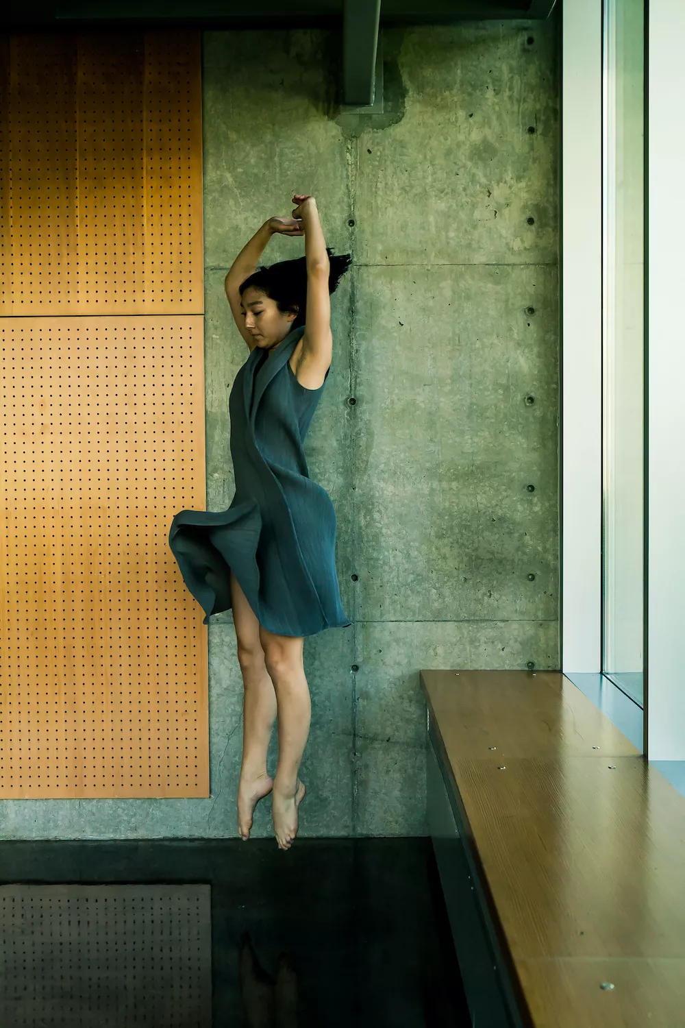 A dancer in a gray dress hovers above the ground in mid jump.
