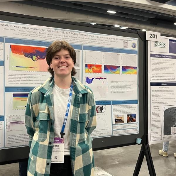Emma Martin smiling and standing in front of her poster display with information on her research.