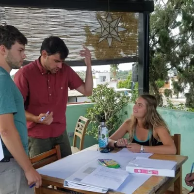4 students sitting and standing around a table discussing research.