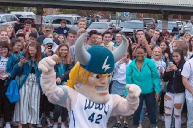 A Viking mascot poses in the center of a large crowd of students, many wearing blue and white clothing.