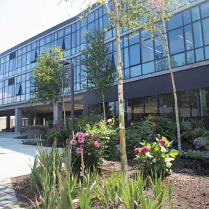 Large L shaped building with lots of windows stands tall against a blue sky. The grounds are nicely landscaped