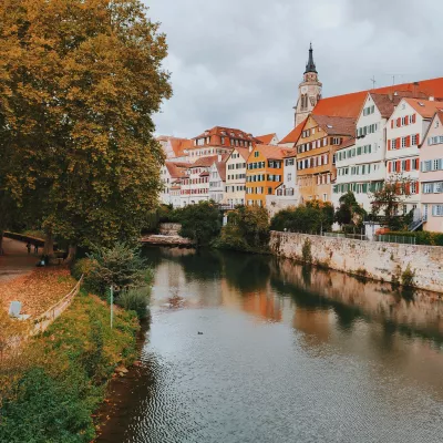 Timber-framed German houses along a river canal. On the other side of the river is a park with large trees and a walking path.