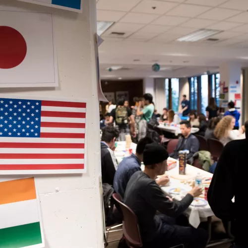 Several flags sit at the door to a room filled with students.