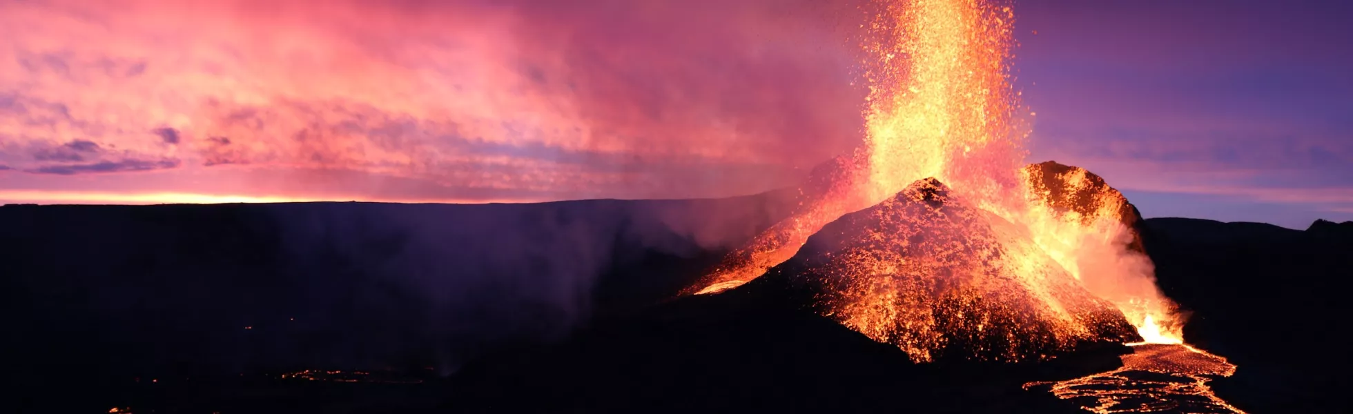 Icelandic volcano erupting lava against a beautiful pink and blue sunset.