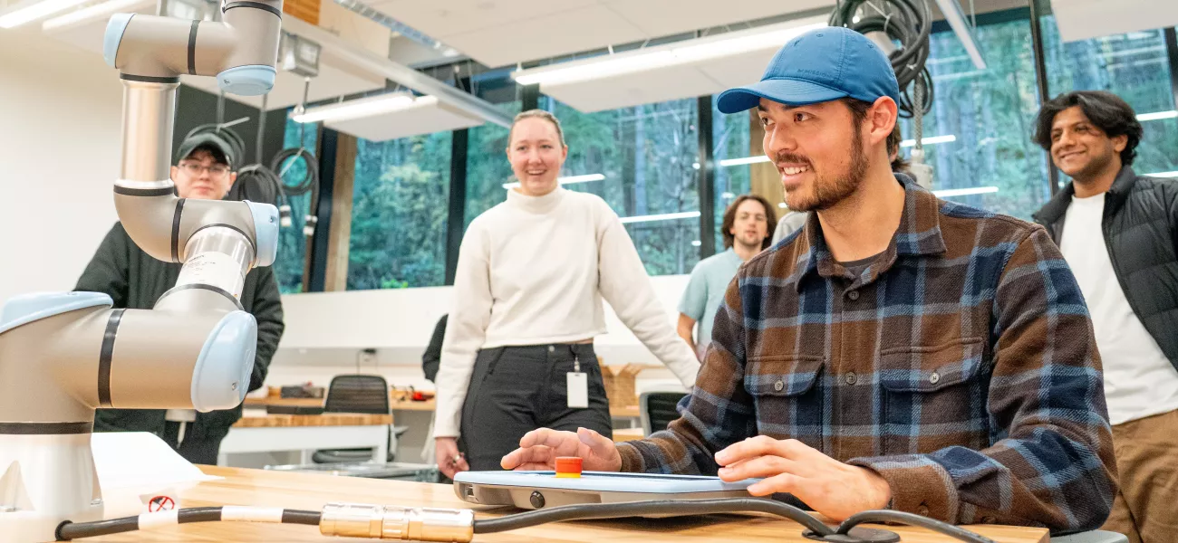 A student in a blue cap operates a robotic arm in a bright, modern lab at Western Washington University. 