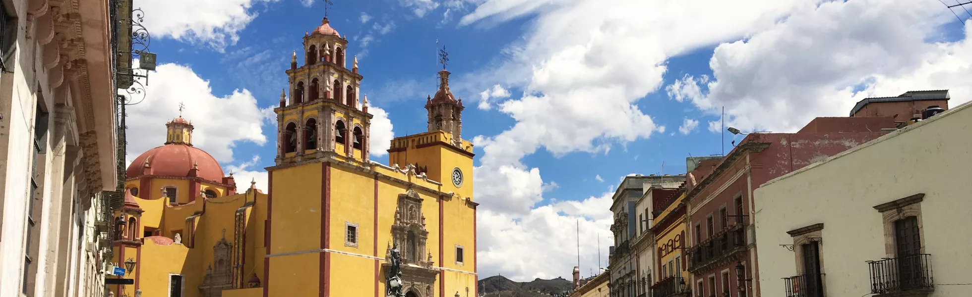 Streets of a city on a sunny day, with a yellow cathedral centered in shot