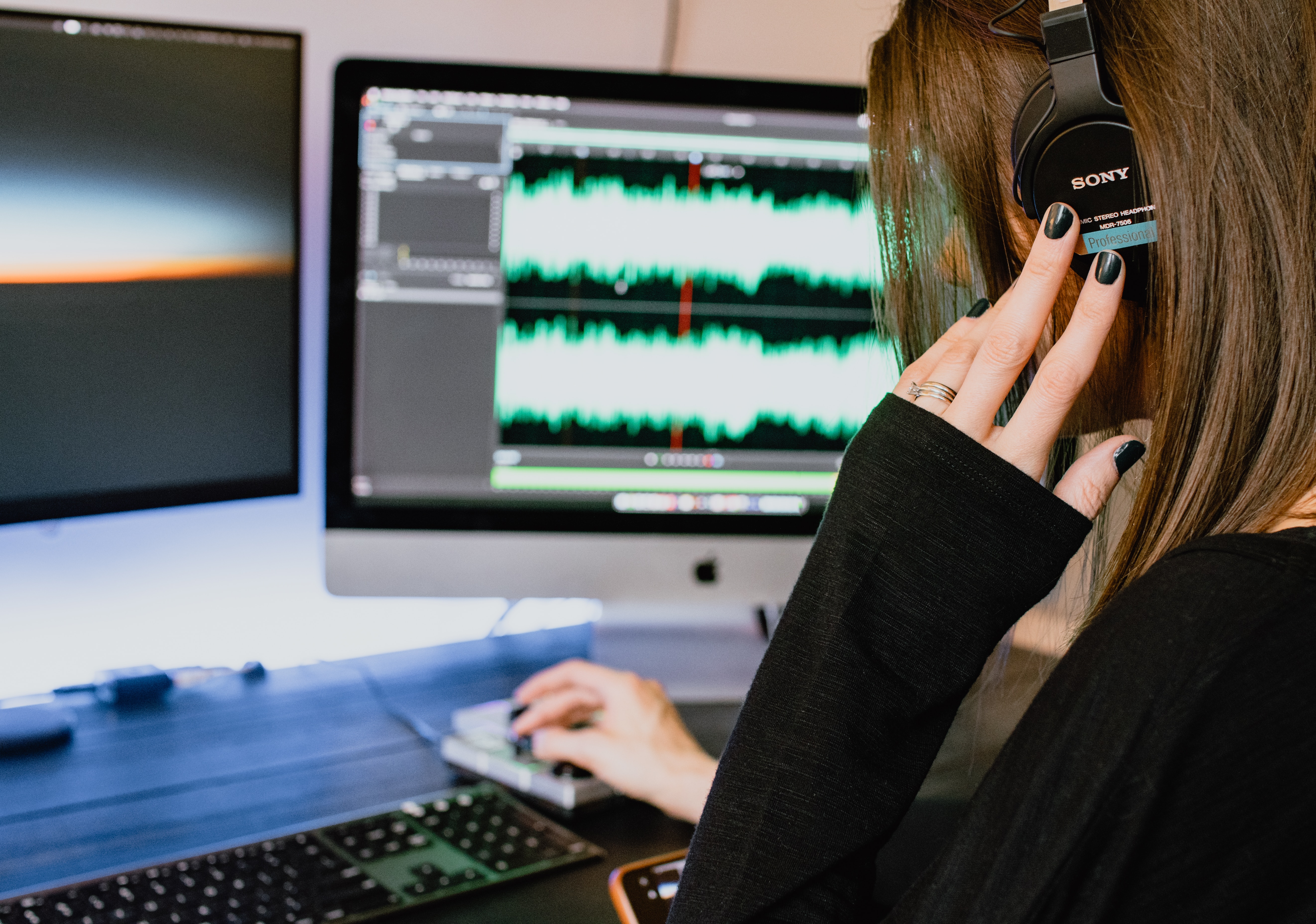 A young person wearing headphones sitting at a computer displaying audio frequencies