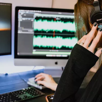 A young person wearing headphones sitting at a computer displaying audio frequencies