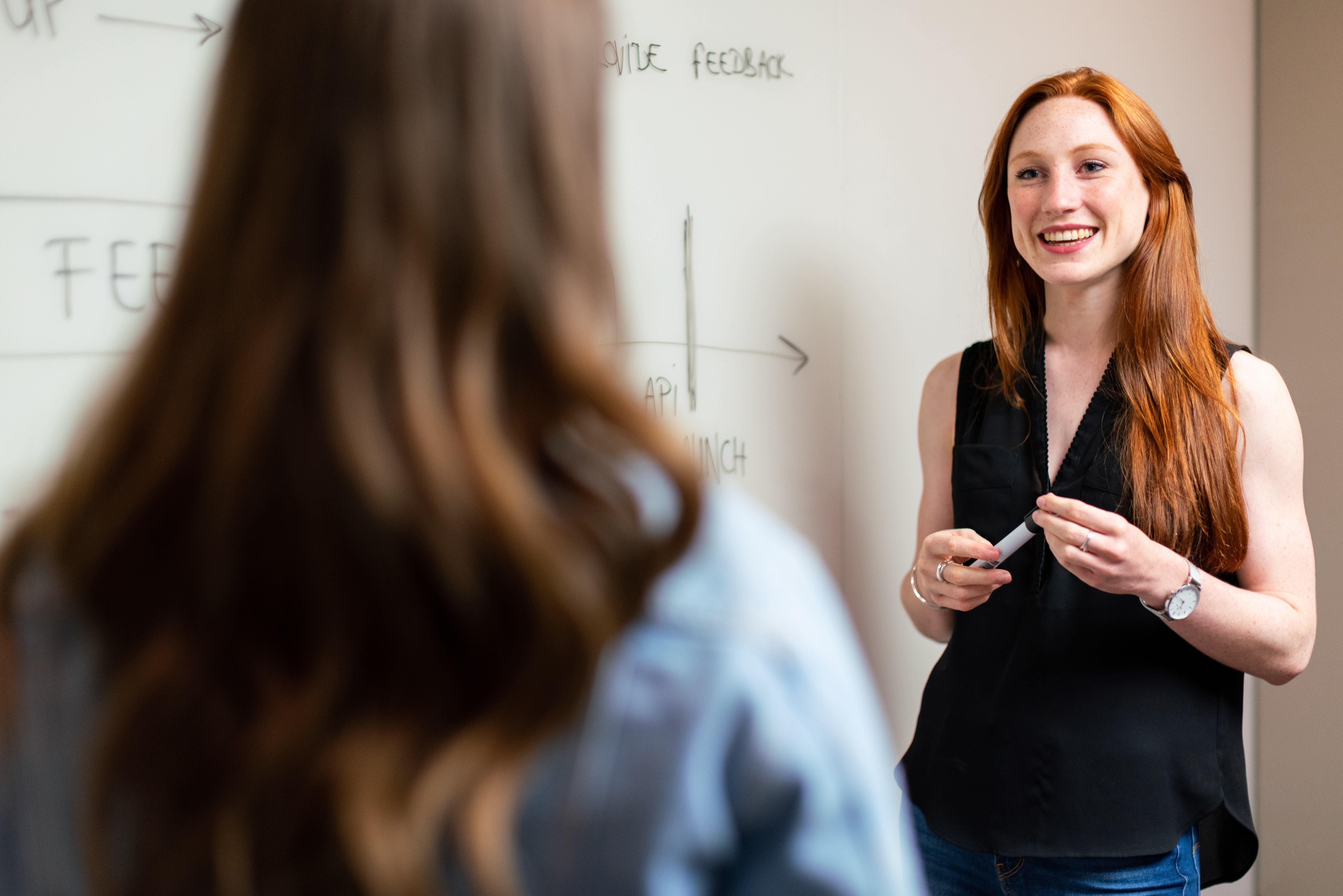 A teacher at a whiteboard in conversation with a person whose back is to the camera