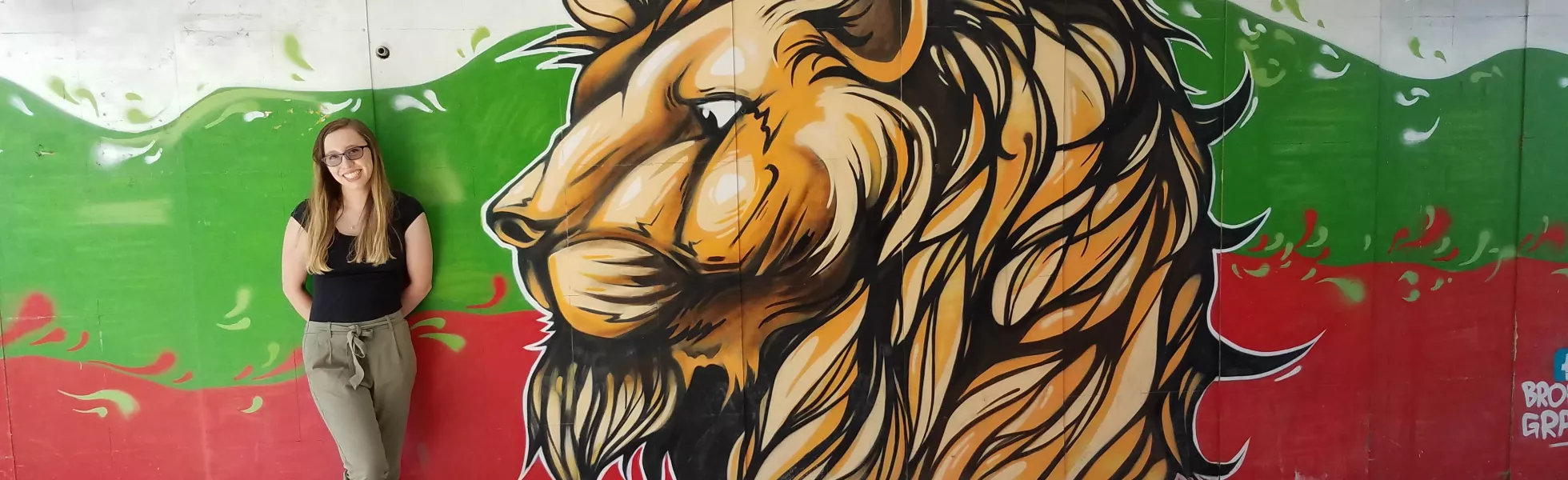 Student standing next to a painted mural of a lion's head in Plodiv, Bulgaria.