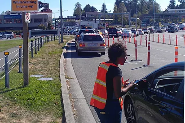 Person in a high-visibility orange vest directing someone in a car