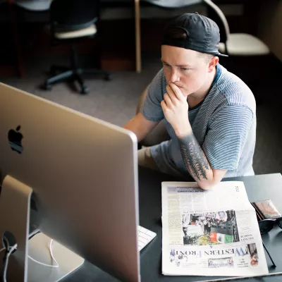 Student sitting at a desktop, thinking and writing, with a copy of the Western Front next to them on their desk.