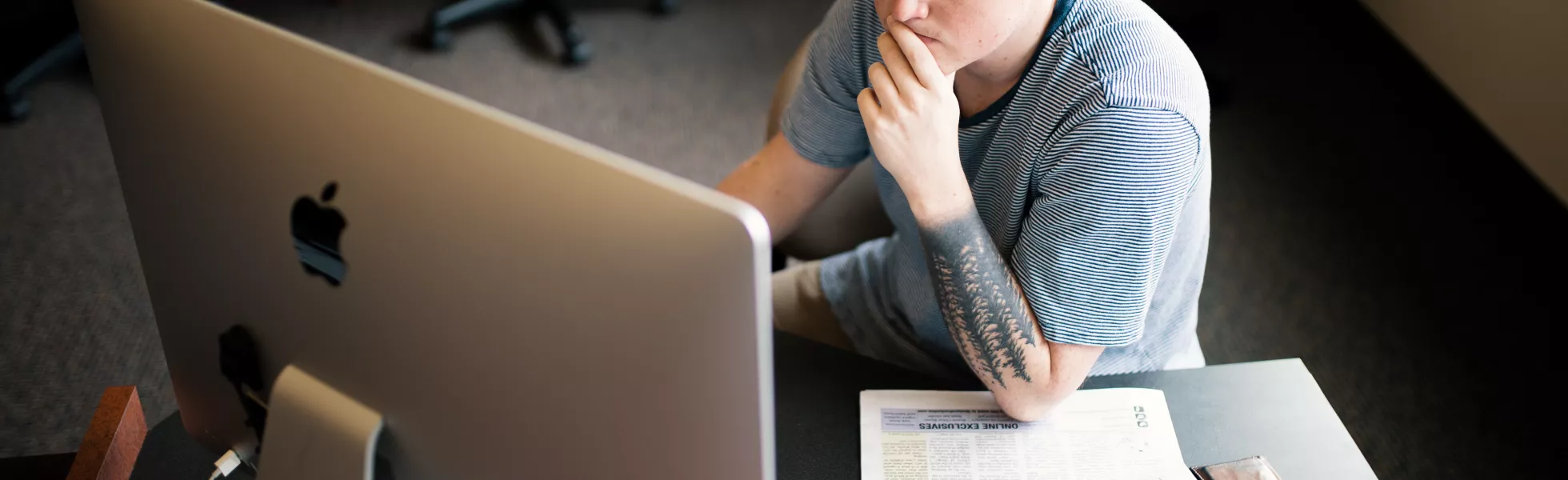 Student sitting at a desktop, thinking and writing, with a copy of the Western Front next to them on their desk.